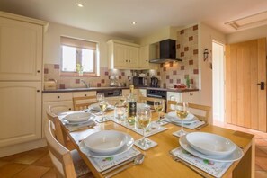 A modern kitchen with white cabinets, a wooden dining table set for four, and a window above the sink.