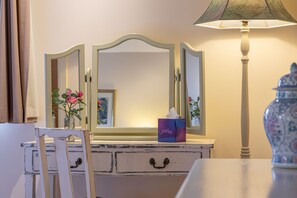 Una stanza con una cassettiera bianca, uno specchio, un vaso con fiori, un portatovaglioli e una lampada.