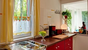 Eine Küche mit Gasherd, einer Kaffeemaschine, Obstschale und einem Fenster mit Vorhängen.