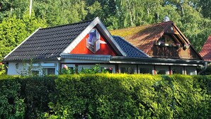 Ein traditionelles Gebäude mit geneigtem Dach, einer sichtbaren Satellitenschüssel und einer gepflegten Hecke davor.