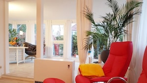 Ein modernes Wohnzimmer mit roten Sesseln, einem Glastisch und einer großen Pflanze in einem Topf.