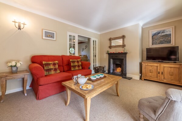 A living room with a red sofa, a wooden coffee table, a fireplace, and a television. - Columbine Cottage, Holme-next-the-Sea, Norfolk (Hunstanton)