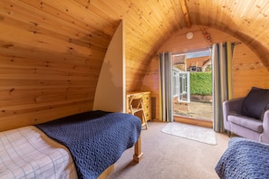 A cozy attic bedroom with wooden walls, a bed, a chair, and a view of a garden through a glass door. - Columbine Cottage, Holme-next-the-Sea, Norfolk (Hunstanton)