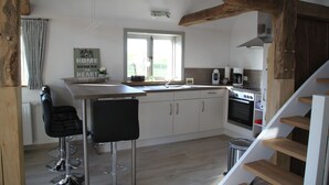 A modern kitchen with white cabinets, a central island with bar stools, a built-in oven, and a window with curtains. - Apartment on the Elbe dyke in Radegast I (Bleckede)