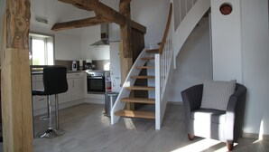 A modern kitchen with white cabinets, a wooden staircase, and a bar area with a black chair. - Apartment on the Elbe dyke in Radegast I (Bleckede)