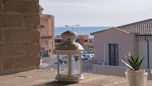 Un balcón con un farol, una planta en maceta y vistas al mar y edificios.