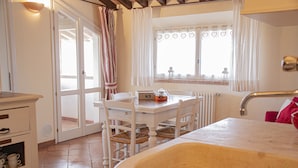 Una cocina con un lavamanos, armarios blancos, una mesa de comedor con sillas y una ventana con cortinas.