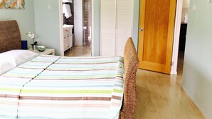 Una camera da letto con un letto, un comodino, e un bagno visibile attraverso una porta aperta, oltre a una porta in legno.