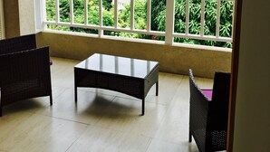 Un balcone con mobili in vimini, un tavolo in vetro e vista sul mare e sulla vegetazione.