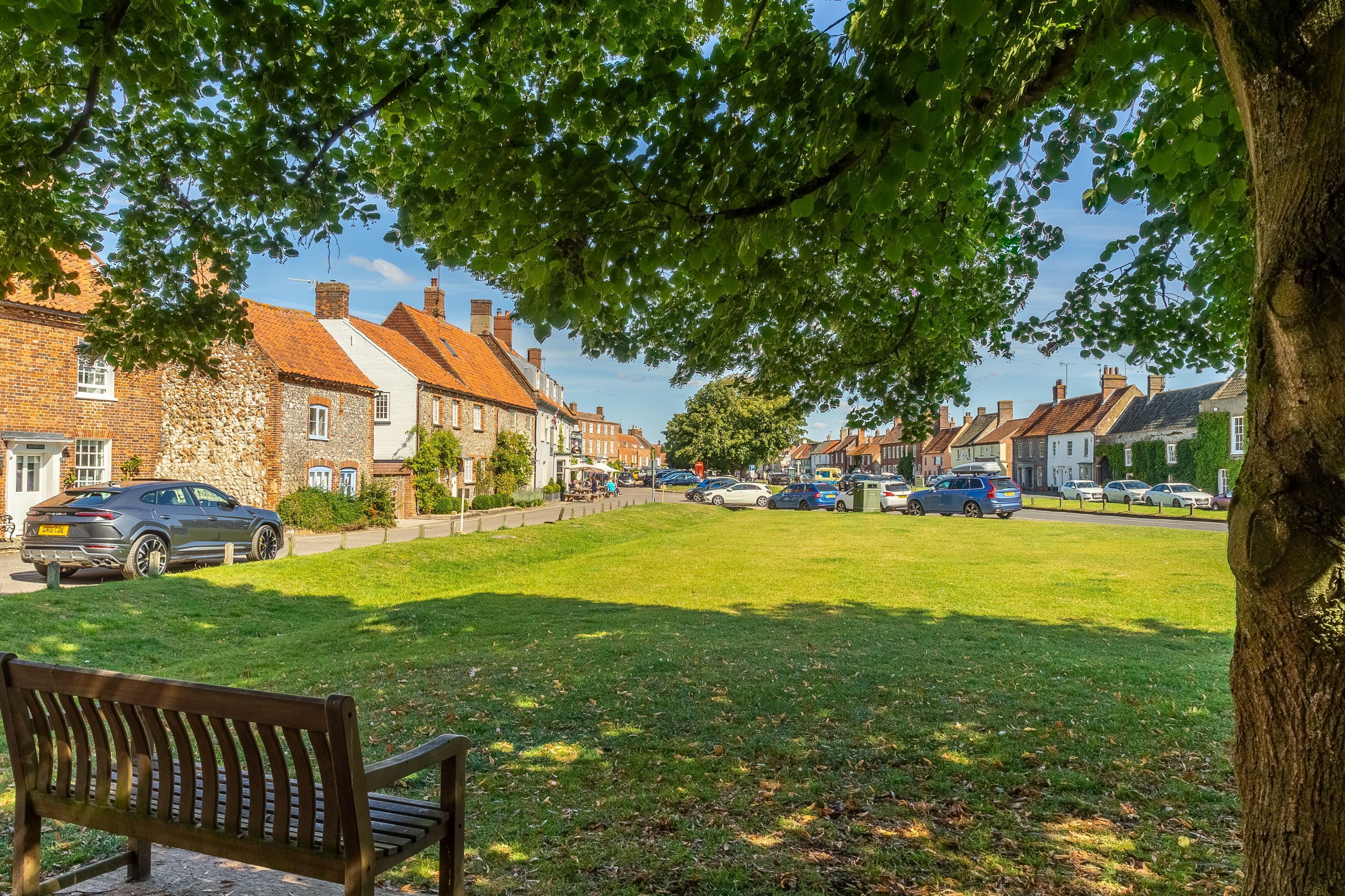 A park with a bench, a grassy area, and a row of houses with brick and stone facades.