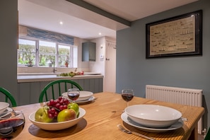 A dining area with a wooden table set for two, a bowl of fruit, and wine glasses. - 4 Gravel Hill, Burnham Overy Town, Norfolk (King's Lynn)