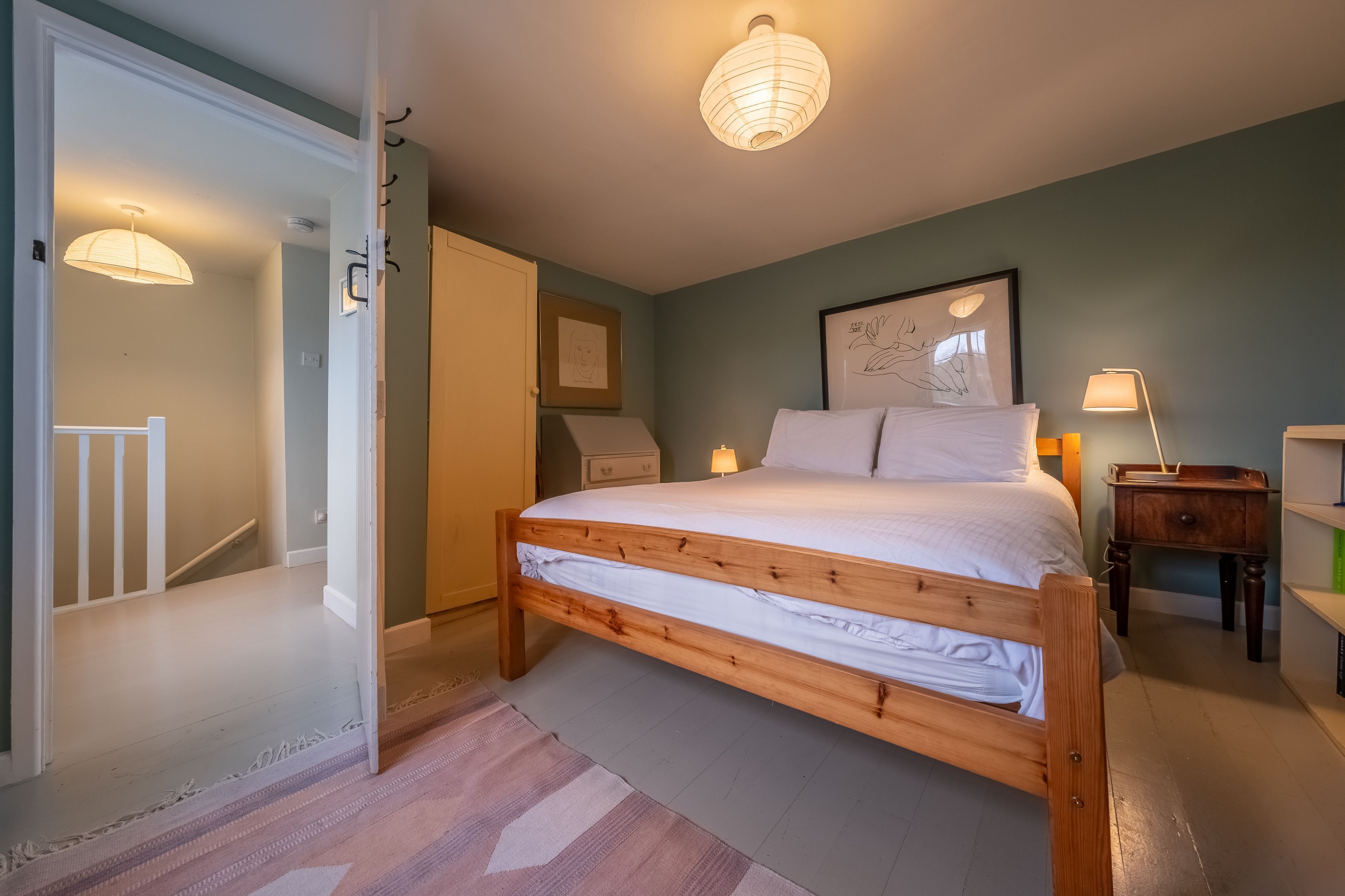 Um quarto com cama de madeira, mesa de cabeceira, luminária e quadro na parede.