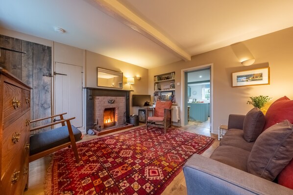 A cozy living room with a fireplace, a sofa, a patterned rug, and a wooden cabinet.