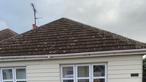 Una casa de un solo piso con techo de tejas, revestimiento blanco y entrada de grava.