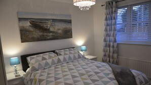 Un dormitorio con una cama, dos mesitas de noche con lámparas, un cuadro de un barco en la pared y una ventana con persianas.