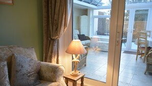 Una sala de estar con sofá, una lámpara y un ventanal corredera que da a un patio exterior con sillas y una mesa.