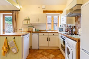 A compact kitchen with a dishwasher, oven, and washing machine, featuring a tiled backsplash and wooden cabinets.