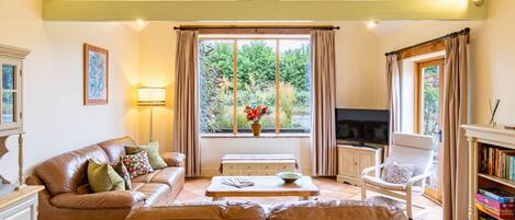 A living room with a sofa, a television, a bookshelf, and a window with curtains.