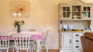 A dining area with a table set for four, chairs, a vase with flowers, and a cabinet with glass doors. - The Cart Lodge, Great Massingham, Norfolk (King's Lynn)