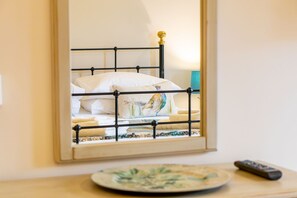 Een bed met een metalen frame, een kussen met een vogelprint, een afstandsbediening en een bord op een houten tafel.