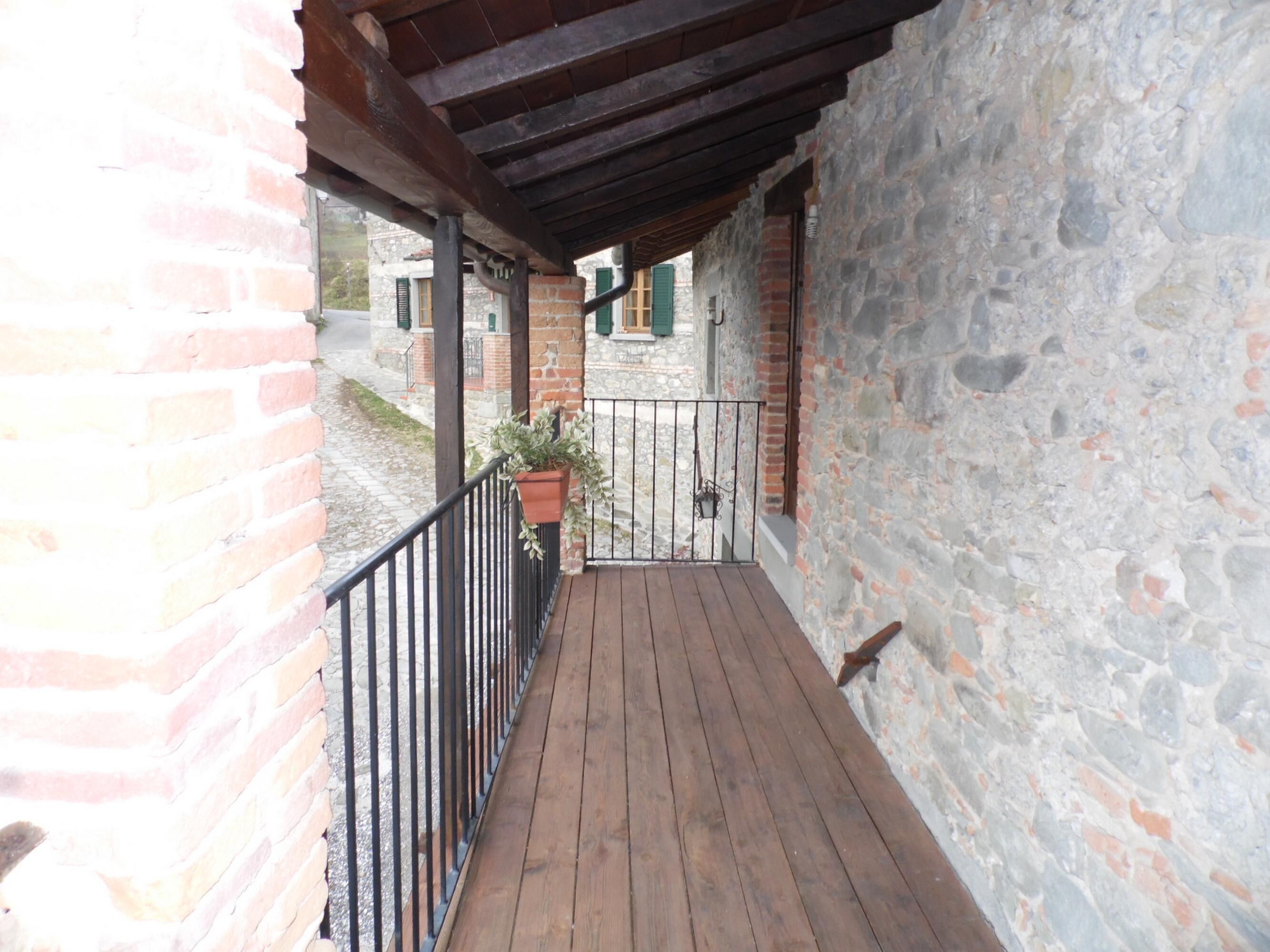 A wooden balcony with stone walls and a metal railing.