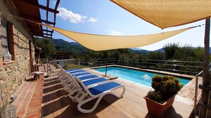 Un espace piscine avec des chaises longues bleues, une terrasse en bois et une vue sur les montagnes.