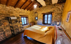 A bedroom with a stone wall, wooden beams, a bed with a yellow blanket, a fan, and a window with shutters. - Charming Rustic Tuscan Retreat,  Private Pool, Beautiful Garden, stunning views! (Pieve Fosciana)