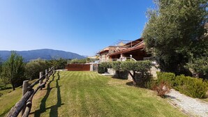 Une maison de campagne en pierre, avec une clôture en bois, une pelouse bien entretenue et une vue sur les montagnes en toile de fond.