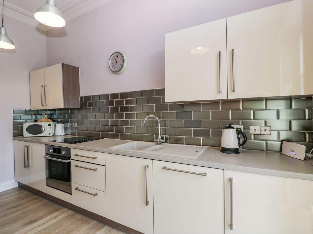 A modern kitchen with a sink, microwave, kettle, and a clock on the wall.