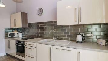 A modern kitchen with a sink, microwave, kettle, and a clock on the wall.