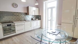 A modern kitchen with a glass dining table, stainless steel appliances, and a brick backsplash. - Ayr Beach View Apartment (Ayr)