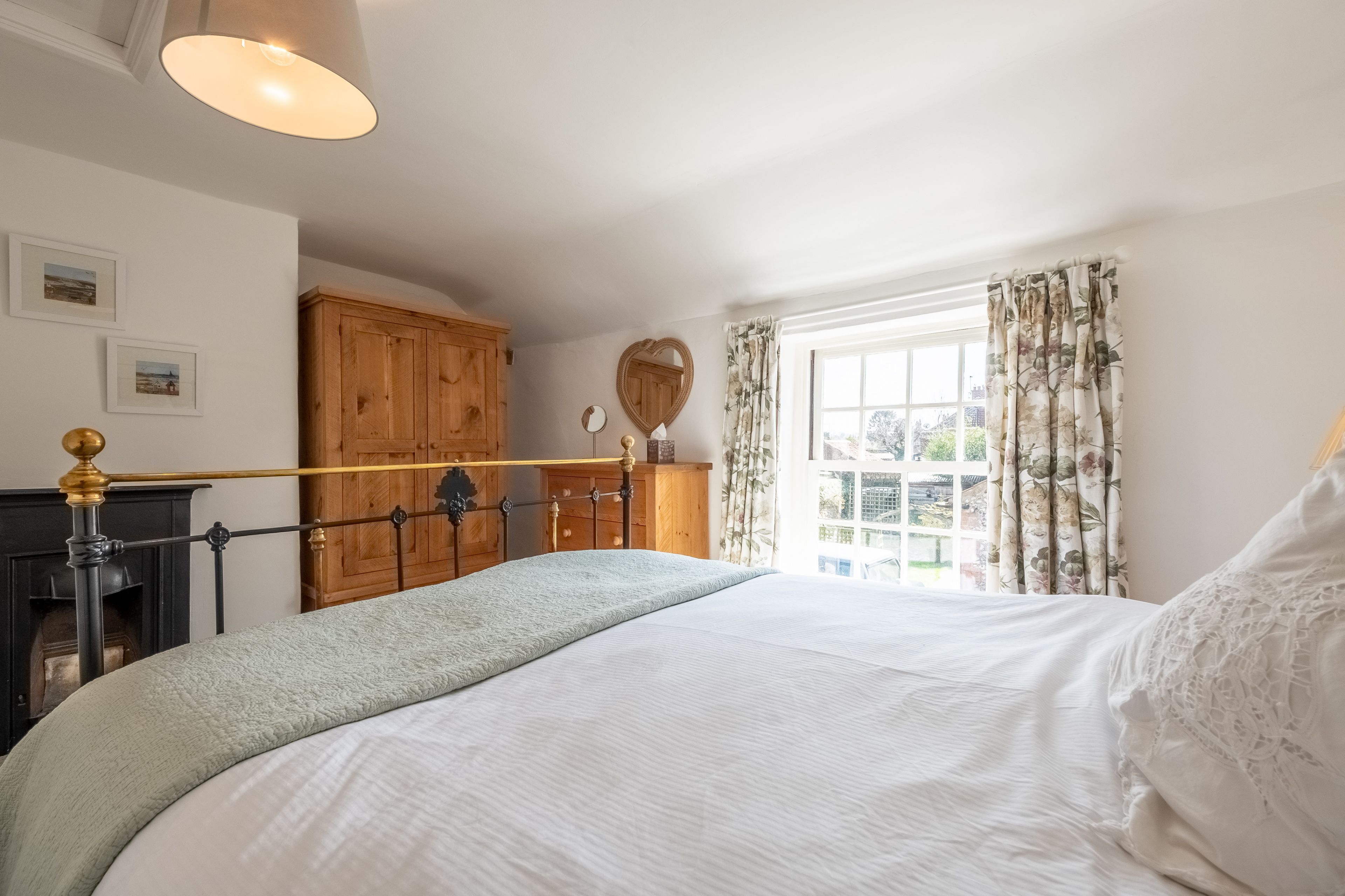 A bedroom with a bed, a wooden wardrobe, a mirror, and a window with curtains.