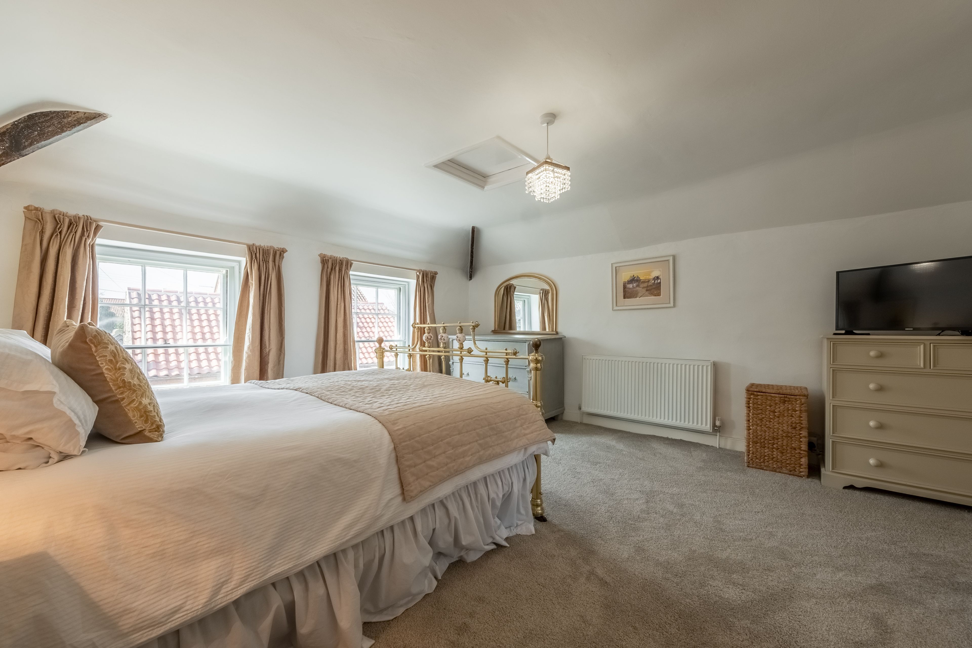 A bedroom with a bed, dresser, vanity, and a television.