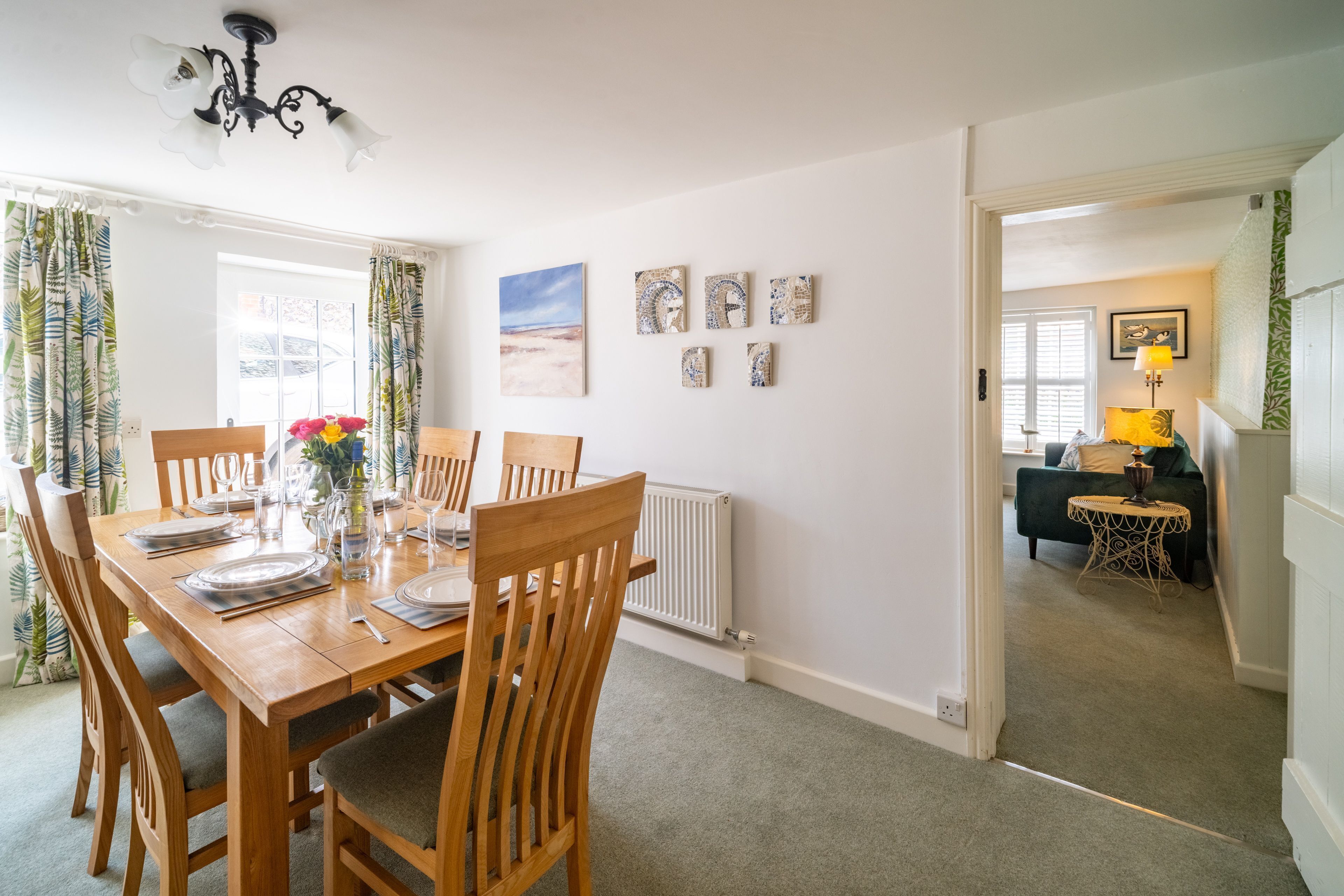 A dining area with a wooden table set for four, chairs, and a chandelier.