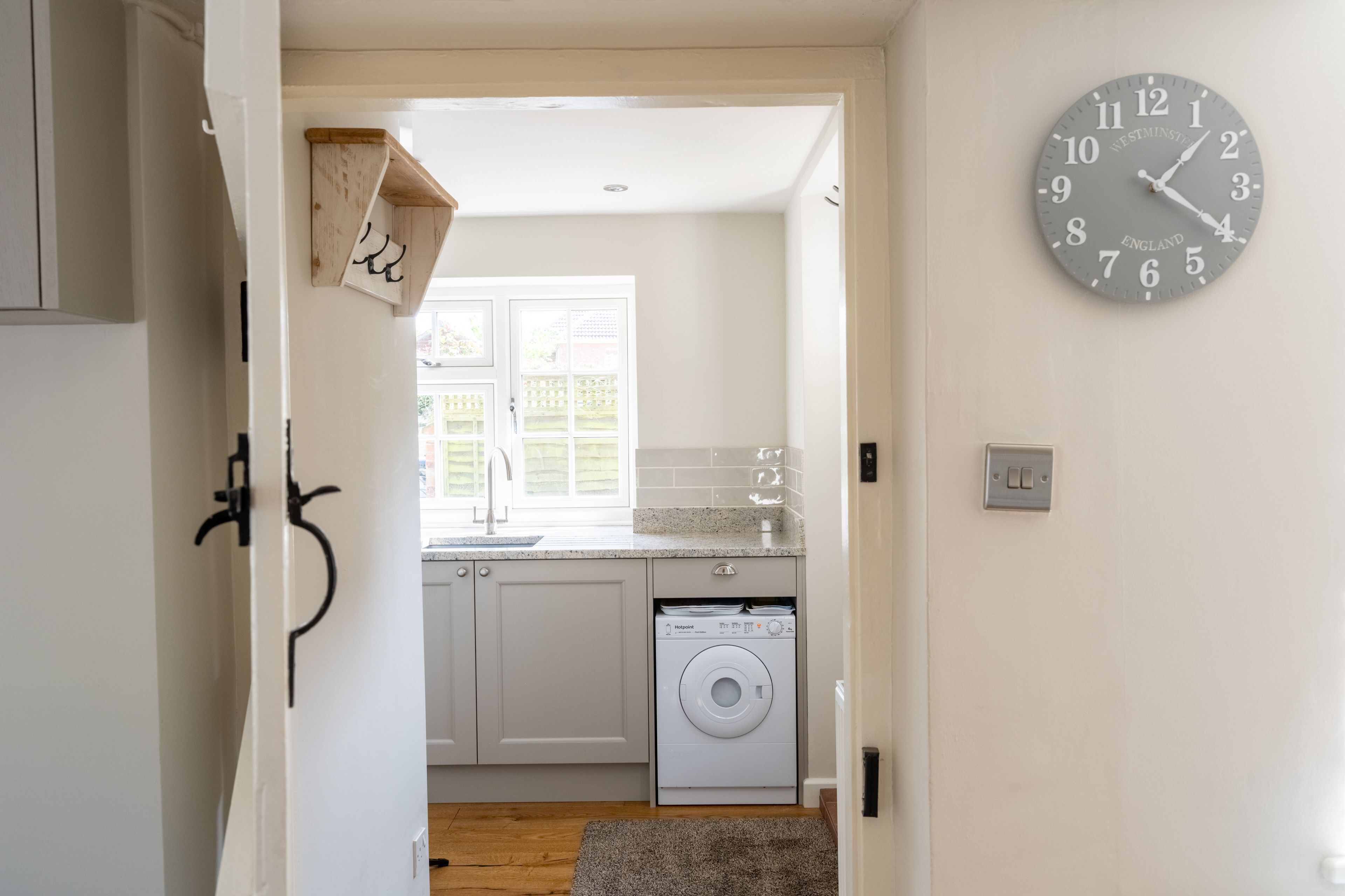 A kitchen with a washing machine, a clock, and a window with a view of a fence.