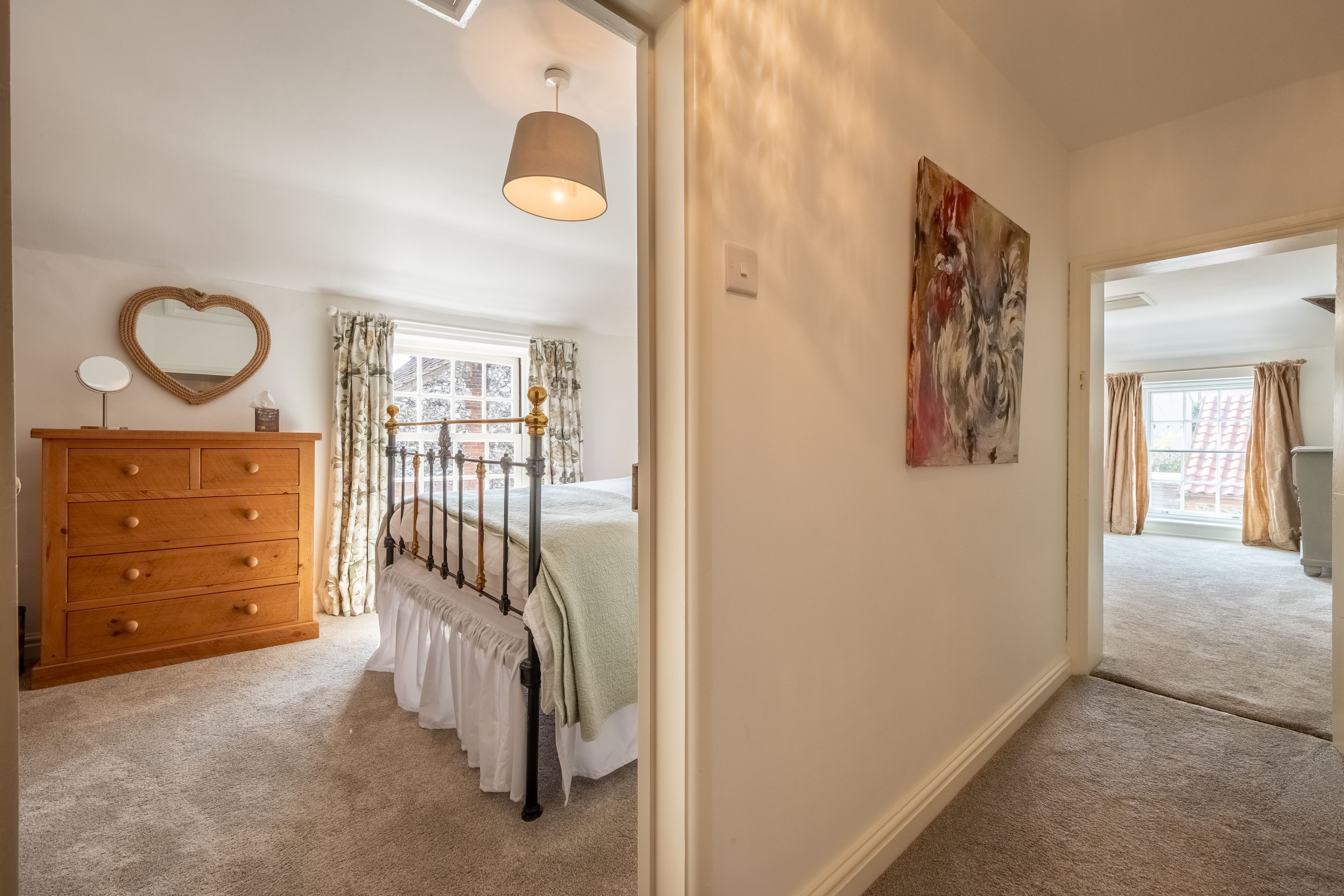 Une chambre à coucher avec un lit, une commode, un miroir et un tableau.