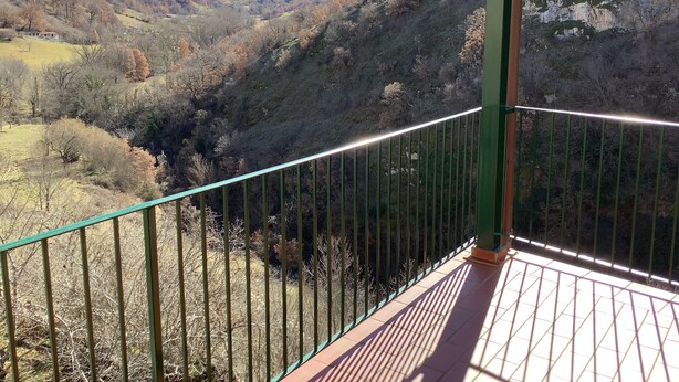 Een balkon met een metalen hekwerk met uitzicht op een bergachtig landschap met een vallei en een rivier.