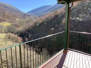 A balcony with a metal railing overlooking a mountainous landscape with a valley and a river.