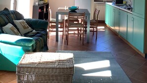 Een gezellige woonkamer met een bank, een eettafel en een keukenhoek met kastjes en een koelkast.