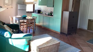 Een compacte keuken met blauwgroene kastjes, een eethoek met een tafel en stoelen, en een kitchenette met een koelkast en magnetron.