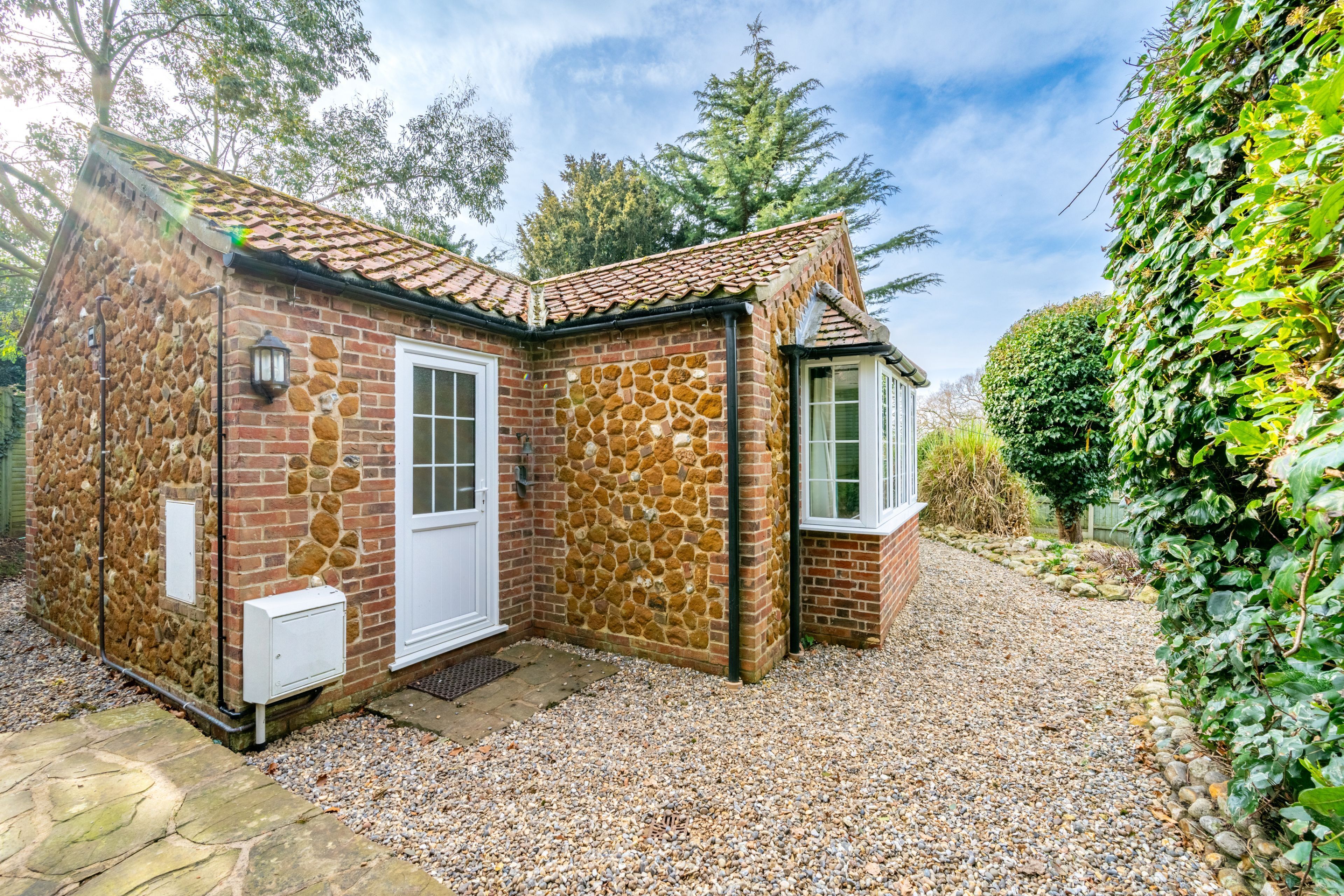 A stone house with a tiled roof, a gravel driveway, and a garden with various plants.