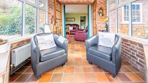 A conservatory with two leather sofas, a brick wall, and a view of the garden.