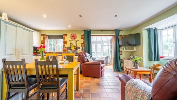 A spacious living area with a dining table, chairs, a sofa, and a TV.