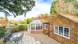 A stone house with a tiled patio, a conservatory, and a garden.