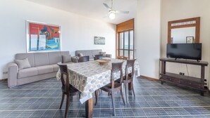 A dining area with a table, chairs, a ceiling fan, a television on a stand, and a sofa. - Cozy apartment Blue Sunset sea view in Gallipoli CVG42 (Gallipoli)