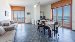 A spacious living area with a sofa, dining table, chairs, a ceiling fan, and large windows with a view of the sea. - Cozy apartment Blue Sunset sea view in Gallipoli CVG42 (Gallipoli)