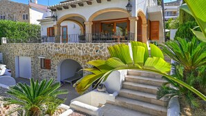 A Mediterranean-style villa with a stone facade, a balcony with outdoor furniture, and a staircase leading to the entrance.