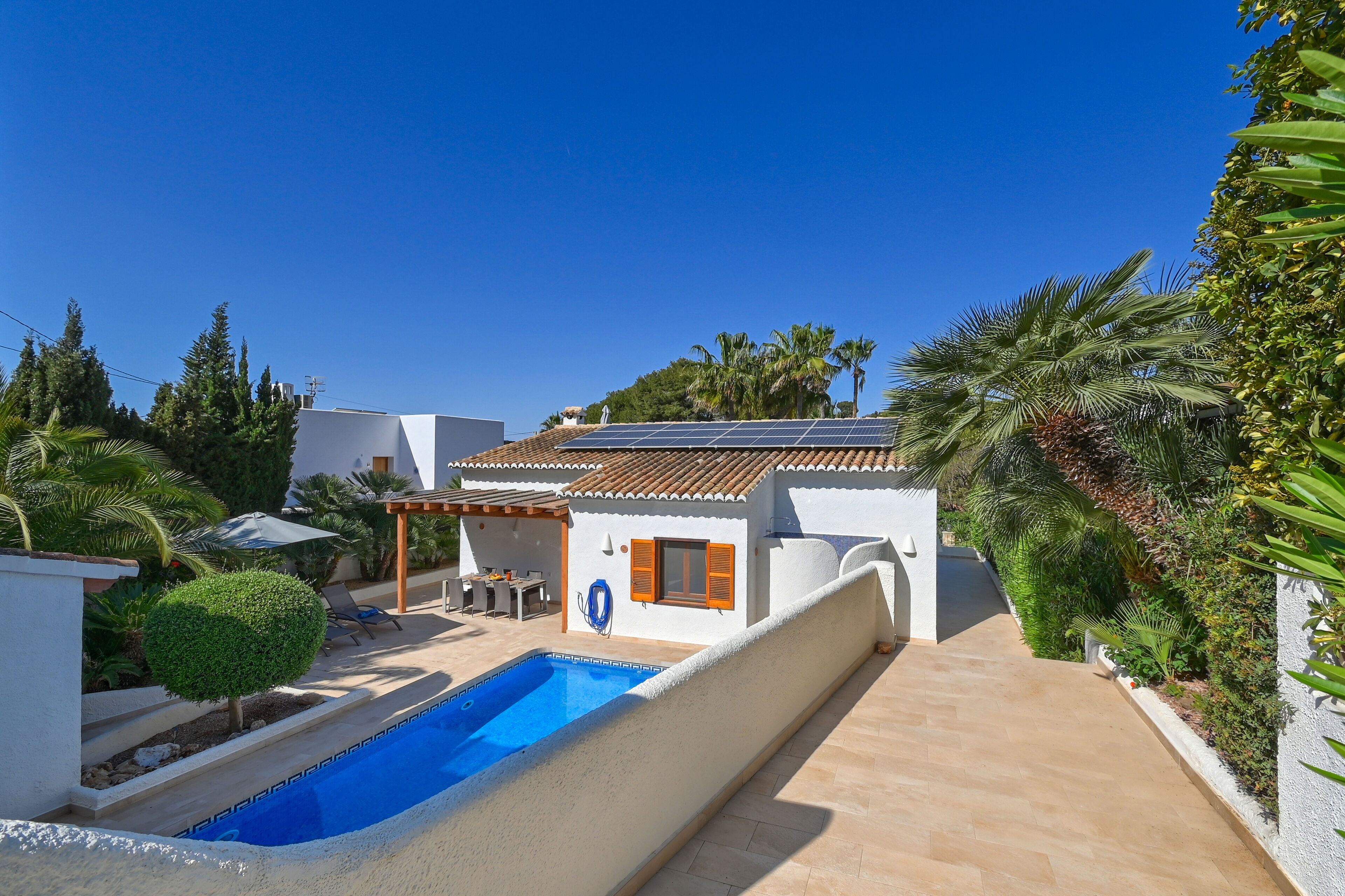 A modern villa with a swimming pool, solar panels, and a patio area.