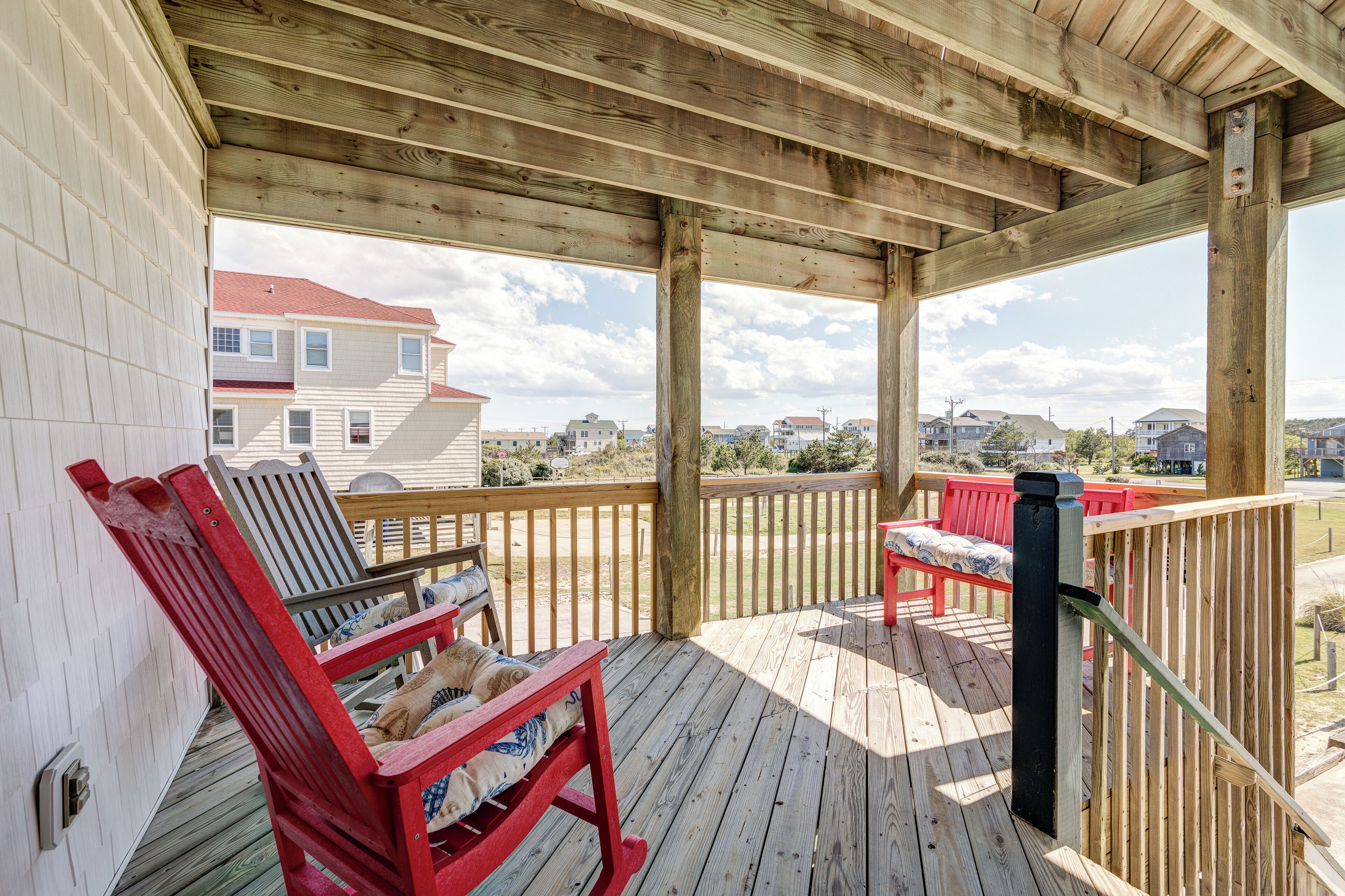A wooden deck with two red Adirondack chairs and a dog lying on one.