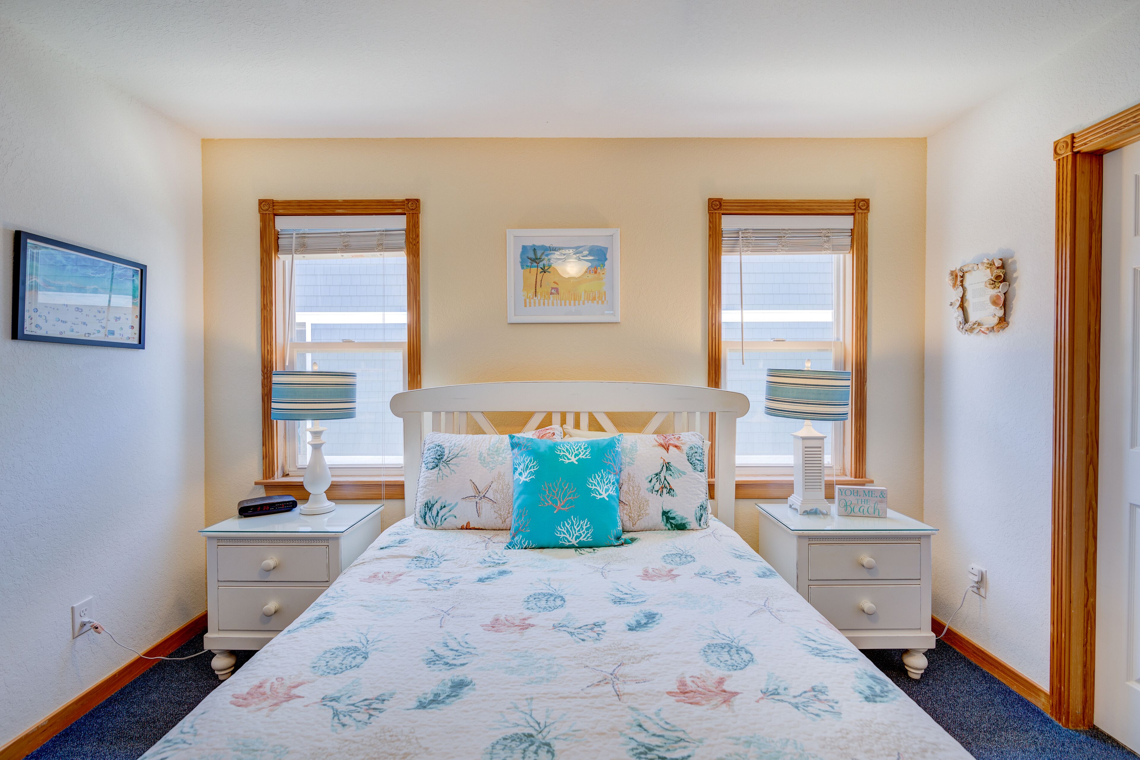 A bedroom with a bed, two bedside tables, a nightstand, a window, and a wall-mounted picture.